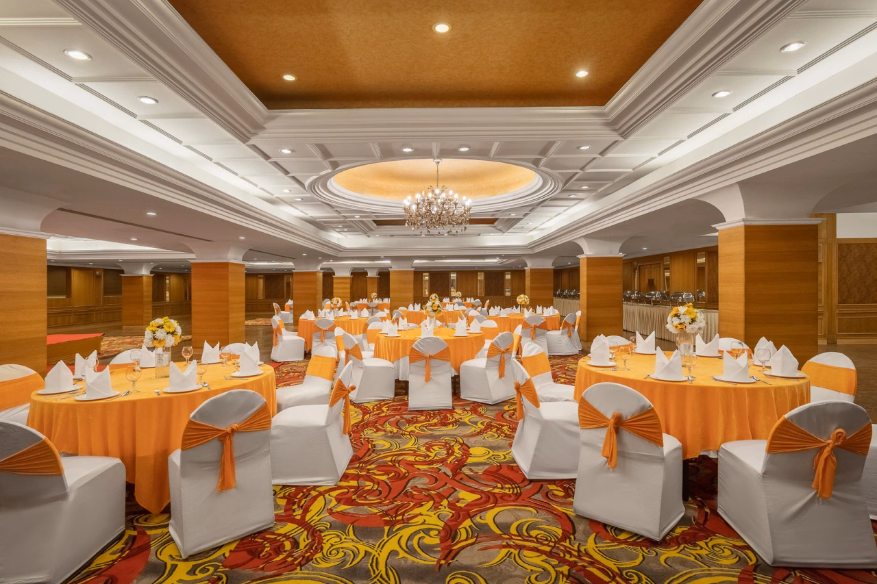 A formal event setup in the Sarovar Portico banquet hall, featuring round tables with white and orange chair covers.